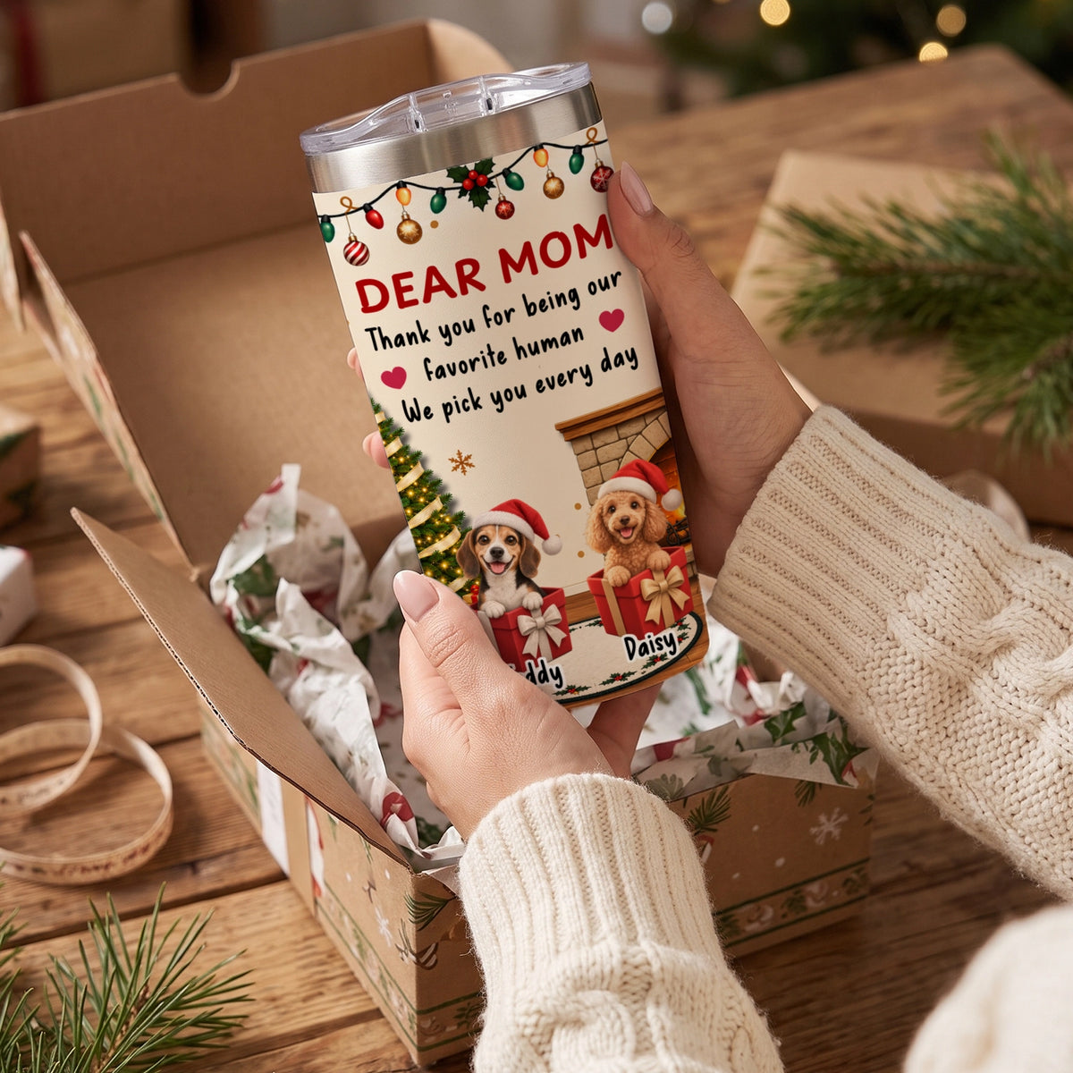Hands holding the Dear Mom tumbler with two cartoon dogs in Christmas gift boxes, one named Daisy