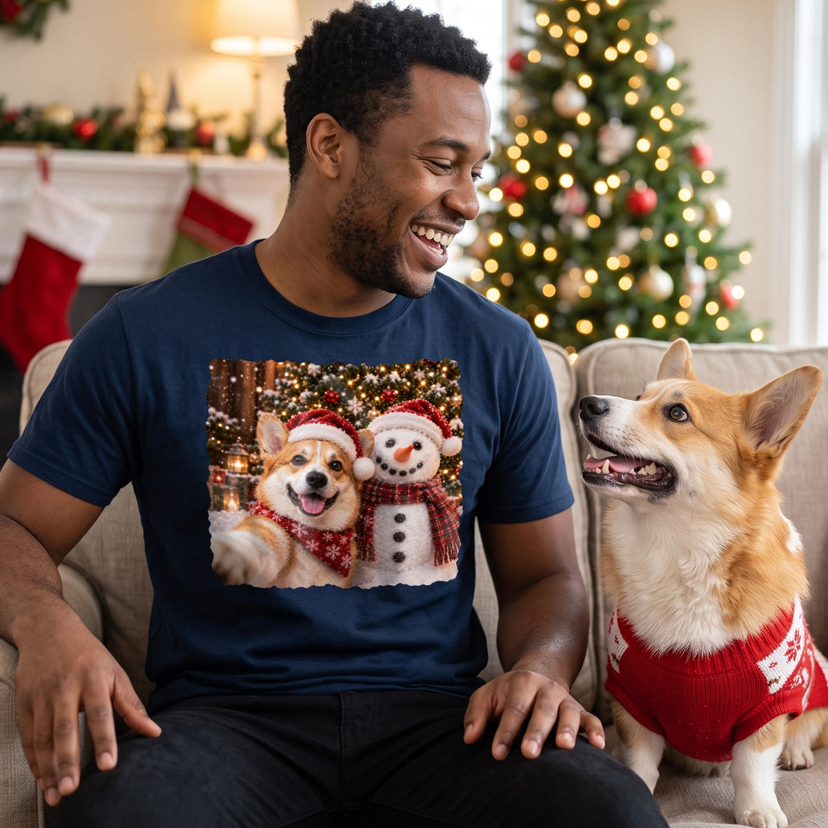 Man in navy Christmas scene T-shirt laughs with his corgi in a red sweater