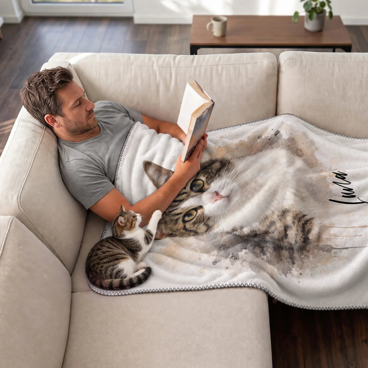 Man reads on the sofa under the Watercolor Cat blanket with his tabby cat