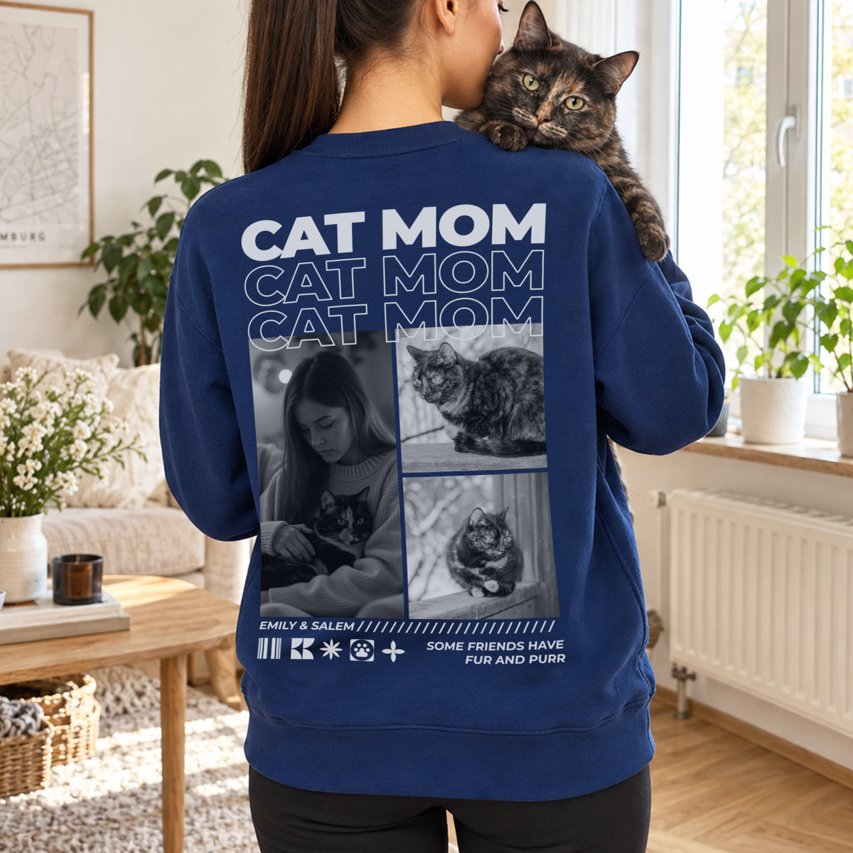 Woman in a navy Cat Mom sweater with a cat on her shoulder by the window