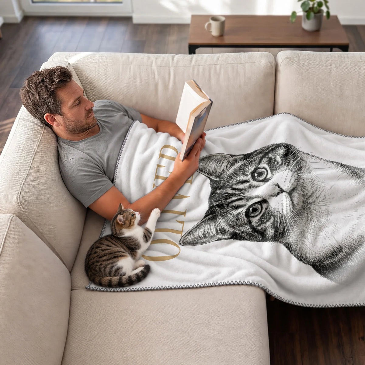 Man reads on the couch under the Retro Cat blanket with his tabby cat