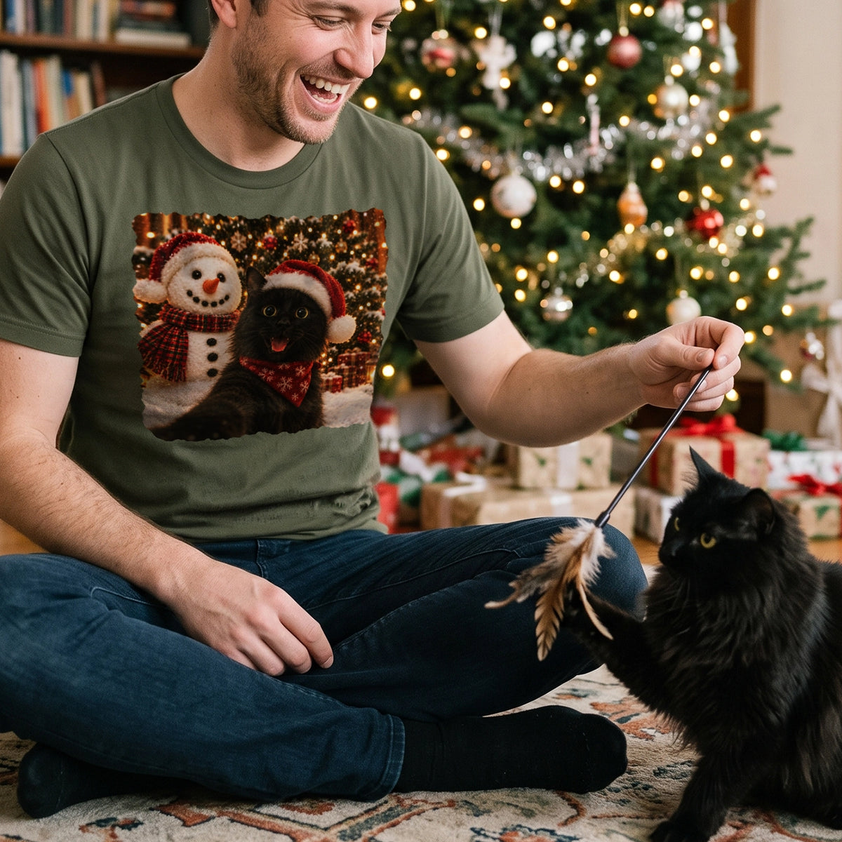 Man in green Christmas T-shirt plays with his black cat by the tree