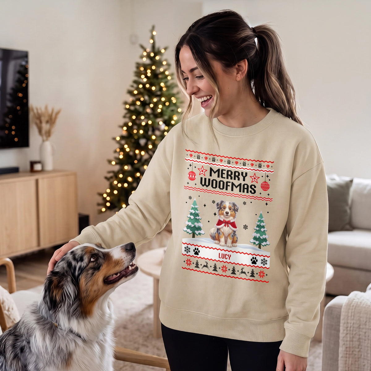 Woman in a sand Merry Woofmas sweater with her Australian Shepherd by the Christmas tree