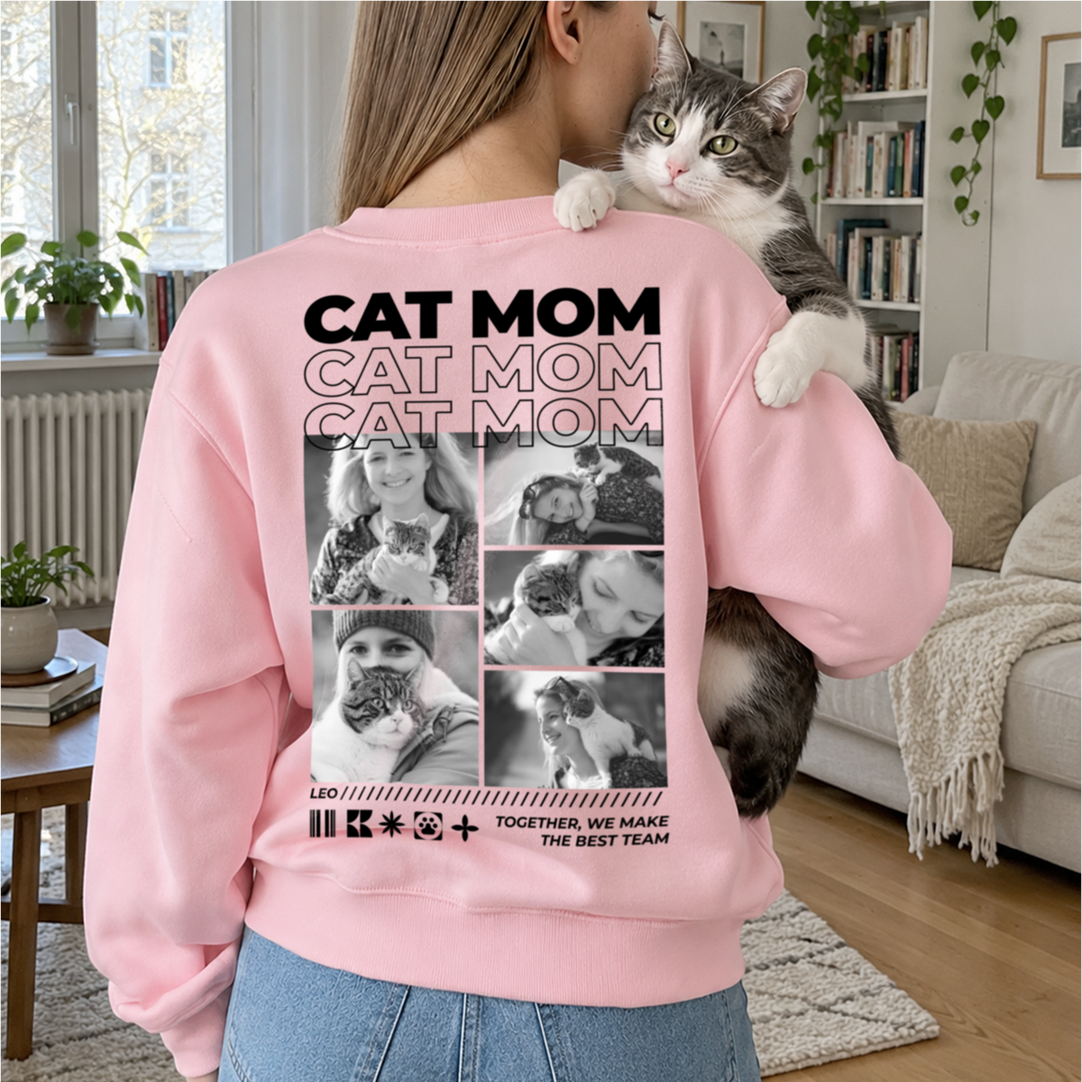 Woman in a pink Cat Mom sweater holding a cat on her shoulder in the living room